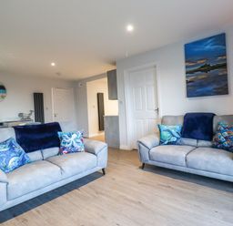 A living room with two grey sofas with blue cushions and a painting on the wall at 2A The Anchorage in Beadnell