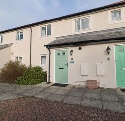 A row of houses with green and white doors and windows and bushes in front at 2A The Anchorage in Beadnell