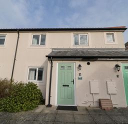 The exterior of a two-story building with light green front doors and windows surrounded by bushes at 2A The Anchorage in Beadnell
