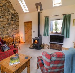 A living room with stone wall a wood stove and checkered armchairs at The Croft in Newtown-Crommelin near Cloughmills