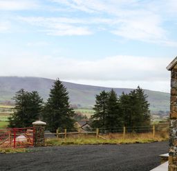 A rural landscape with trees a red metal gate stone pillars and a stone building at The Croft in Newtown-Crommelin near Cloughmills