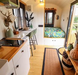 A small kitchen and sleeping area with a stove kettle and coffee machine and a bed with floral bedding at Herdwick Luxury Glamping in Nottingham