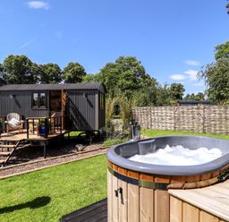 An outdoor area with a hot tub and a raised cabin with stairs and seating at Herdwick Luxury Glamping in Nottingham