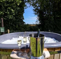 A hot tub with bubbling water outdoors next to a wooden platform holding two champagne glasses and a champagne bottle in an ice bucket at Herdwick Luxury Glamping in Nottingham