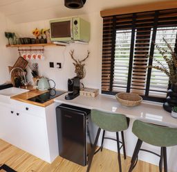 A kitchen area with a sink stove microwave coffee machine small fridge and two green chairs at Southdown Luxury Glamping in Nottingham