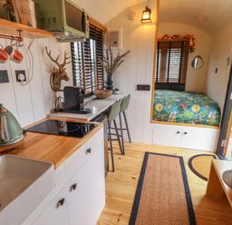 A compact kitchen and dining area with a sink kettle coffee machine stools and a bed with floral bedding at Southdown Luxury Glamping in Nottingham