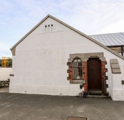 A white building with a wooden door and a small window at East Point Lynas Lighthouse Keeper's Cottage in Llaneilian near Amlwch