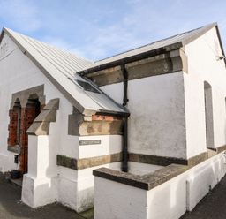A white cottage with a slanted roof and stone trim near a paved area at East Point Lynas Lighthouse Keeper's Cottage Llaneilian near Amlwch
