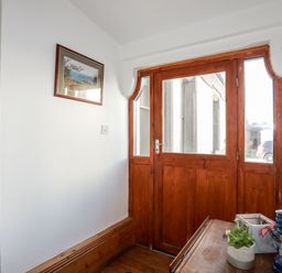 An entryway with a wooden door and window panels a small wooden table with a plant and lantern on it and a framed picture on the wall at East Point Lynas Lighthouse Keeper's Cottage in Llaneilian near Amlwch