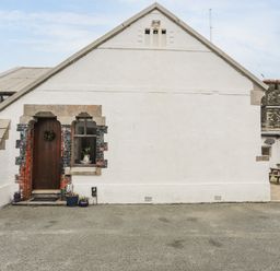 The exterior of a white building with a wooden door, a window, and potted plants near the entrance at West Point Lynas Lighthouse Keeper's Cottage in Llaneilian near Amlwch
