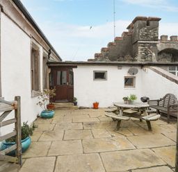 An outdoor patio area with stone flooring wooden picnic table wooden bench potted plants and a wooden gate at West Point Lynas Lighthouse Keeper's Cottage in Llaneilian near Amlwch