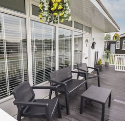 An outdoor patio with black chairs a table hanging flower baskets and potted plants at 39 Cherry Park in Chapel St Leonards