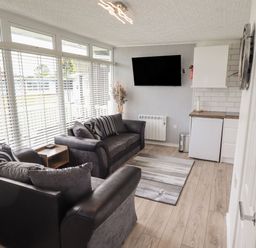 A living room with two sofas a wall-mounted TV and a small kitchen area at 39 Cherry Park in Chapel St Leonards