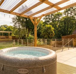 A hot tub on a patio with a pergola and garden area at Ranbir House in Longhope