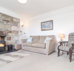 A living room with a stone fireplace a beige sofa a plaid armchair and a framed painting at Crab Pot Cottage in Porthleven