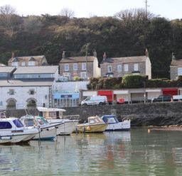 Boats moored in water near a stone wall with buildings and houses behind a wooded hillside at Crab Pot Cottage in Porthleven