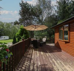A wooden deck with outdoor chairs and table under an umbrella at Kantankye Lodge in Thorpe St Peter near Wainfleet All Saints