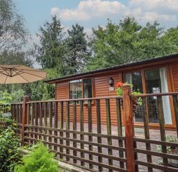 An exterior view of a wooden cabin with a patio and umbrella surrounded by trees and plants at Kantankye Lodge Thorpe St Peter near Wainfleet All Saints