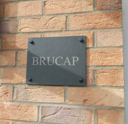 A black rectangular plaque with the word BRUCAP mounted on a brick wall at Brucap Cottage in Beadnell