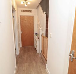 A hallway with a wooden floor a wooden door staircase with a safety gate and a small white shelf with a vase at Brucap Cottage in Beadnell
