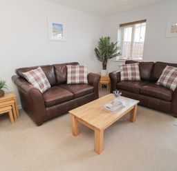 A living room with two brown leather sofas with plaid cushions a wooden coffee table and side tables with plants at Brucap Cottage in Beadnell