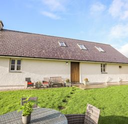 A backyard with outdoor seating and a table with a plant next to a house with a tiled roof at Rhyd Y Bont Bach in Rhoscolyn