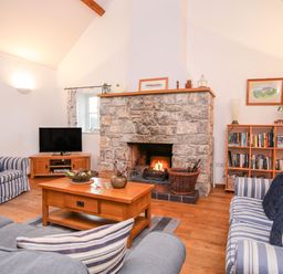 A living room with a stone fireplace wooden furniture striped sofas and a bookshelf at Rhyd Y Bont Bach in Rhoscolyn
