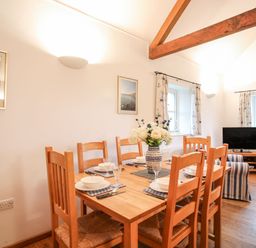 A dining area with a wooden table set for six and a living space with a TV and striped armchair at Rhyd Y Bont Bach in Rhoscolyn
