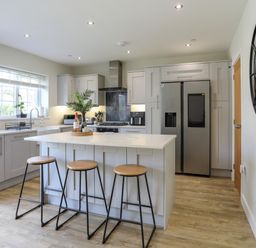 A kitchen with an island and three stools a refrigerator and a round wall mirror at Iscoed in Llangefni