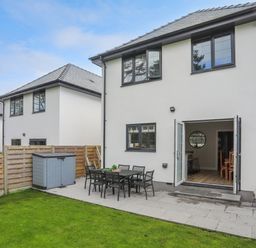 A backyard with a patio table and chairs a storage shed and open double doors leading inside at Iscoed Llangefni