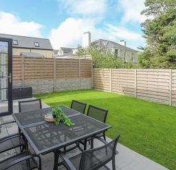 A backyard with a metal table and chairs set on a patio next to a grassy lawn and wooden fence at Iscoed in Llangefni