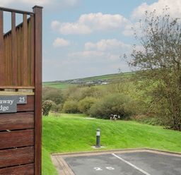 A wooden fence with a Hideaway Lodge sign near a parking space numbered 25 and a grassy field with a cow at Hideaway Lodge Bossiney near Tintagel