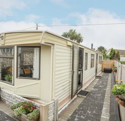 An exterior view of a beige mobile home with a paved walkway and flower pots along the fence at Rhiwlas Bach in Benllech