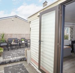 An outdoor patio area with chairs and tables and an open door leading to a living room at Rhiwlas Bach in Benllech