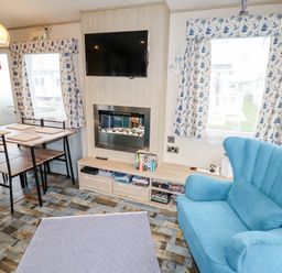 A living room with a blue armchair a wooden dining table with four chairs a wall-mounted tv and a fireplace at Beachcomber D35 in Towyn