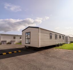 A row of mobile homes on paved and grassy lots under a partly cloudy sky at Beachcomber D35 in Towyn