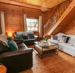 A living room with two leather sofas one fabric sofa a wooden coffee table and a staircase at Glenisle in Dalbeattie