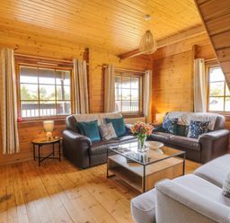 A wooden living room with two leather sofas a fabric sofa a glass coffee table and a side table with a lamp at Glenisle in Dalbeattie
