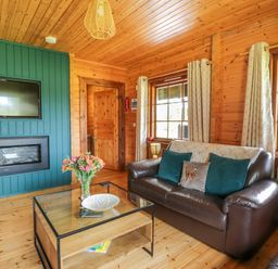 A living room with leather sofas a glass coffee table and a wall-mounted TV at Glenisle in Dalbeattie