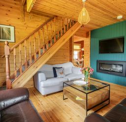 A living room with a wooden staircase a sofa a coffee table flowers and a fireplace at Glenisle in Dalbeattie