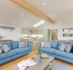 An open plan living room and kitchen with two blue sofas and a wooden coffee table at 4 Valley View in Lanreath