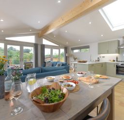 A kitchen and dining area with a wooden table set with food and drinks a blue sofa and large windows in the background at 4 Valley View in Lanreath