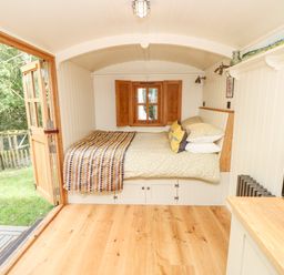 A small room with a bed under a window and wooden floor with open doors leading outside at The Happy Hut in Sopley near Christchurch