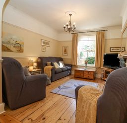 A living room with armchairs a sofa a wooden floor a rug a window with curtains and a television at Green Gate Cottage in Reydon near Southwold