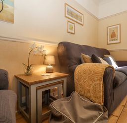 A living room with a sofa throw pillows side tables a lamp and wall art at Green Gate Cottage Reydon near Southwold