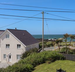 A white house near the ocean with green bushes and a lawn at Seaside Sanctuary in Trearddur Bay