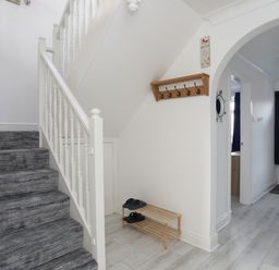 A hallway with stairs carpeted in grey and a wooden shoe rack under the stairs at Seaside Sanctuary in Trearddur Bay