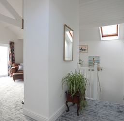 A hallway with a plant on a wooden stand and stairway with skylight and paintings at Seaside Sanctuary in Trearddur Bay