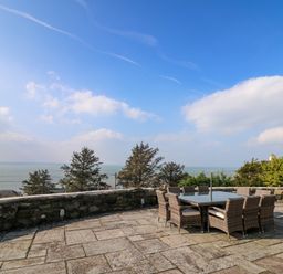 An outdoor patio with a table and chairs overlooking trees and the sea at Mynydd ar Mor in Barmouth