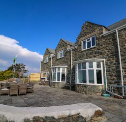An outdoor patio area with stone paving and wicker dining furniture outside a stone house with large windows at Mynydd ar Mor in Barmouth